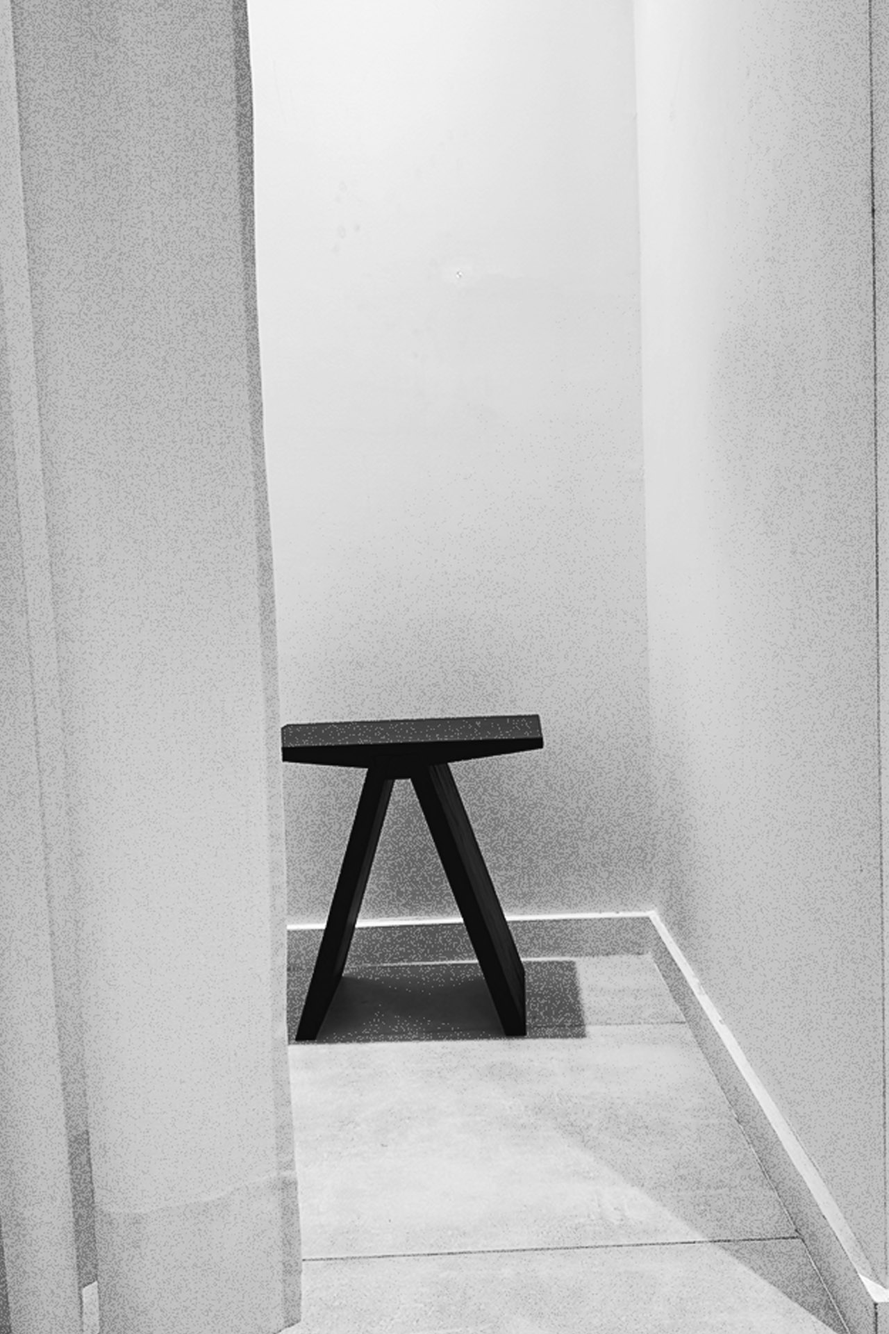 Minimal black stool placed between pale architectural walls