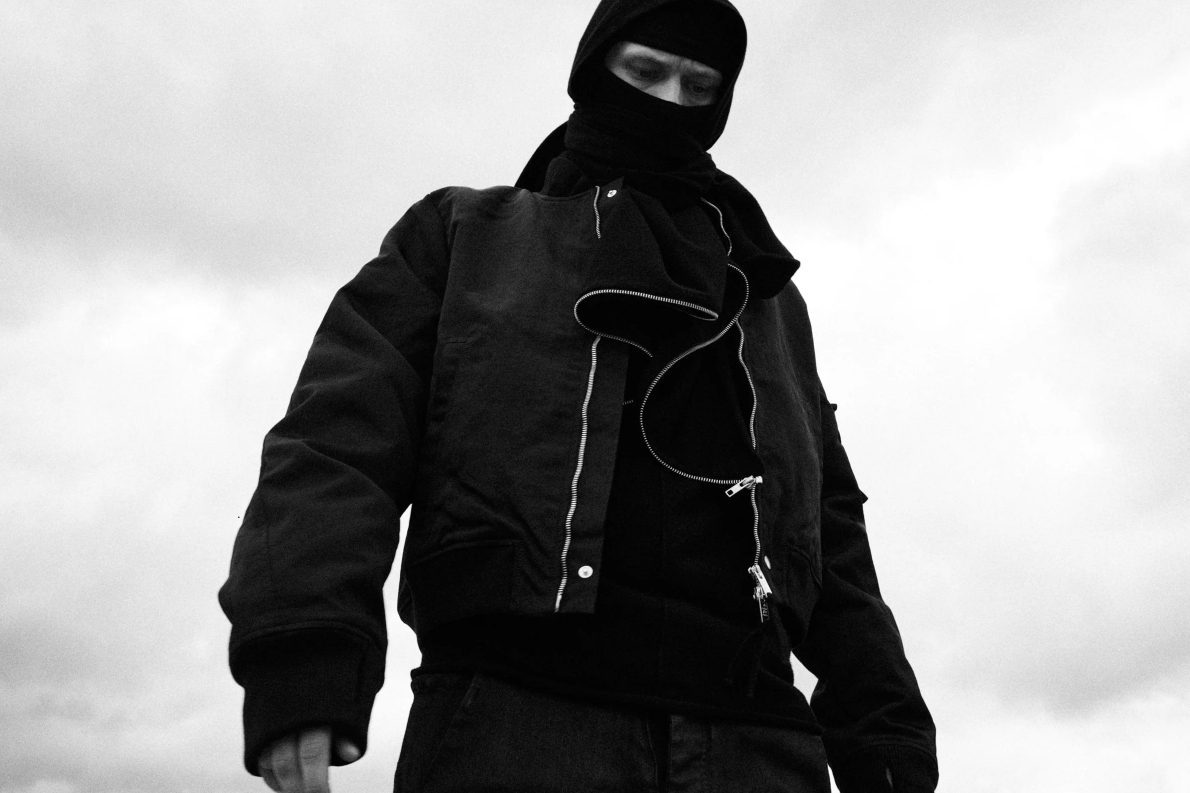 Black architectural outfit against a raw wall